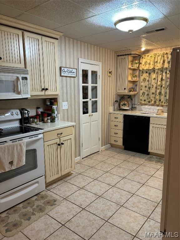 kitchen featuring white appliances, light tile patterned floors, a drop ceiling, and cream cabinetry