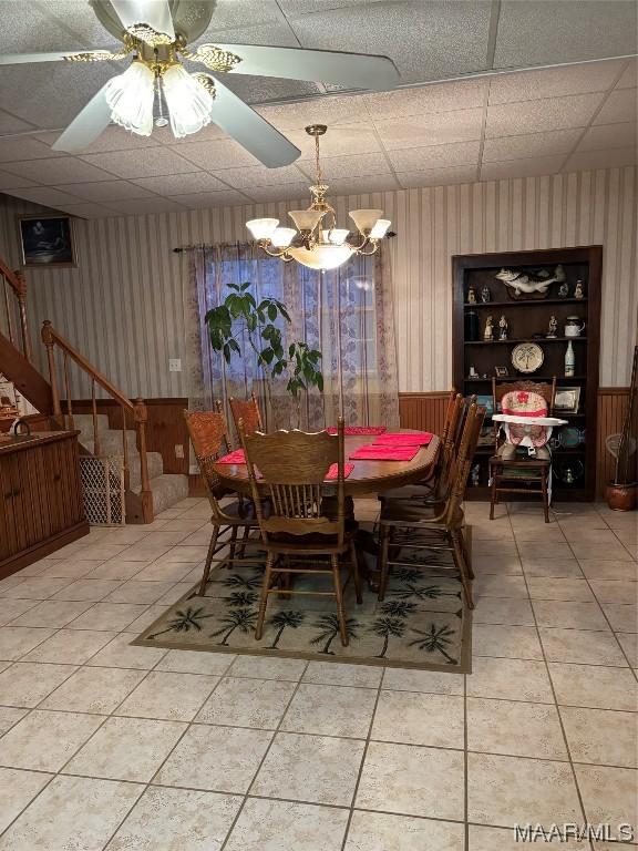 dining space with tile patterned flooring, a paneled ceiling, a notable chandelier, and wooden walls