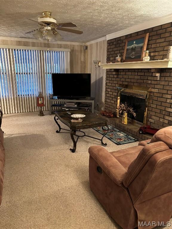 living room with a brick fireplace, a textured ceiling, ornamental molding, carpet flooring, and ceiling fan