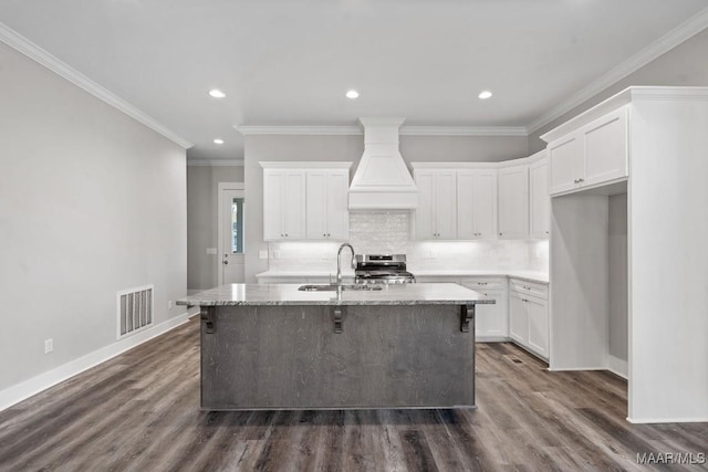 kitchen with a kitchen island with sink, custom range hood, sink, and white cabinets