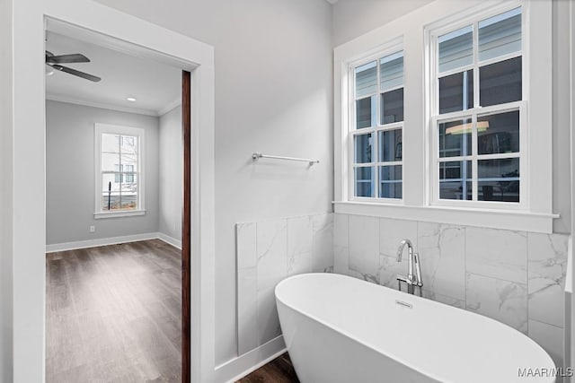 bathroom with tile walls, ornamental molding, a bathing tub, ceiling fan, and hardwood / wood-style floors