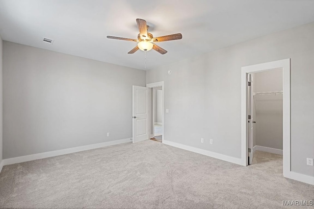 unfurnished bedroom with ceiling fan, a spacious closet, light carpet, and a closet