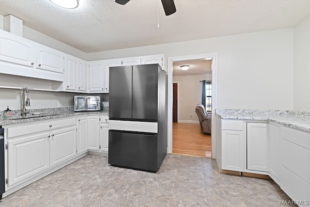 kitchen with white cabinetry, sink, stainless steel fridge, and a textured ceiling