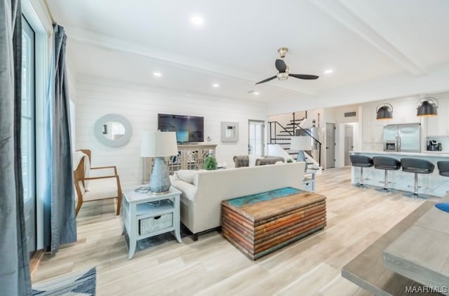 living room featuring beam ceiling, ceiling fan, and light wood-type flooring