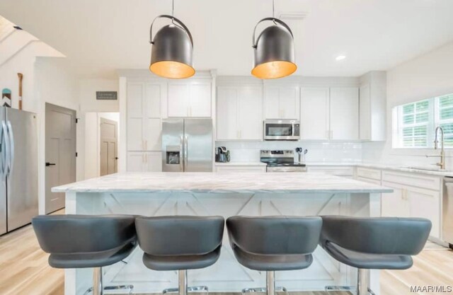 kitchen with appliances with stainless steel finishes, white cabinets, a kitchen island, light stone countertops, and backsplash