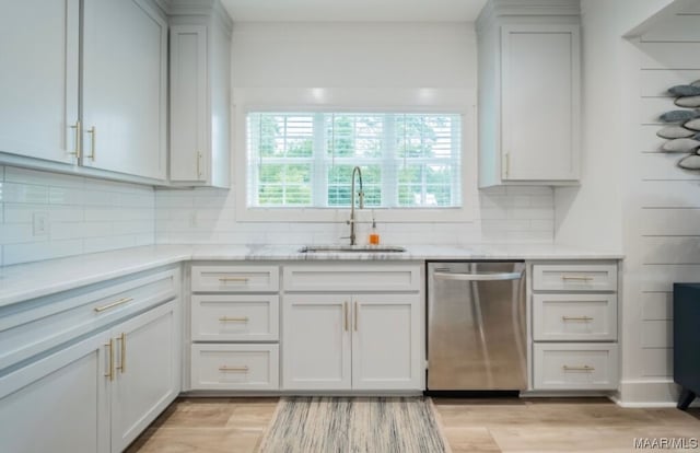 kitchen with tasteful backsplash, stainless steel dishwasher, sink, and light hardwood / wood-style flooring