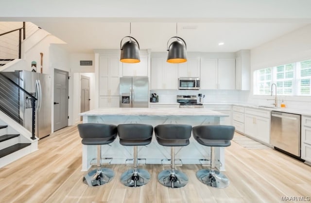 kitchen with white cabinetry, backsplash, appliances with stainless steel finishes, light hardwood / wood-style floors, and a center island