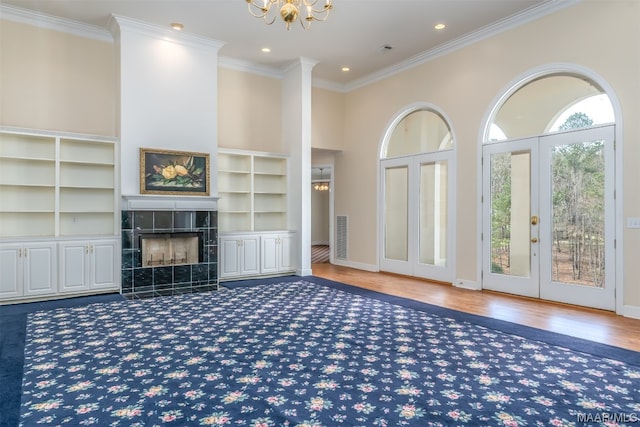 unfurnished living room with crown molding, hardwood / wood-style flooring, built in features, a tile fireplace, and a chandelier