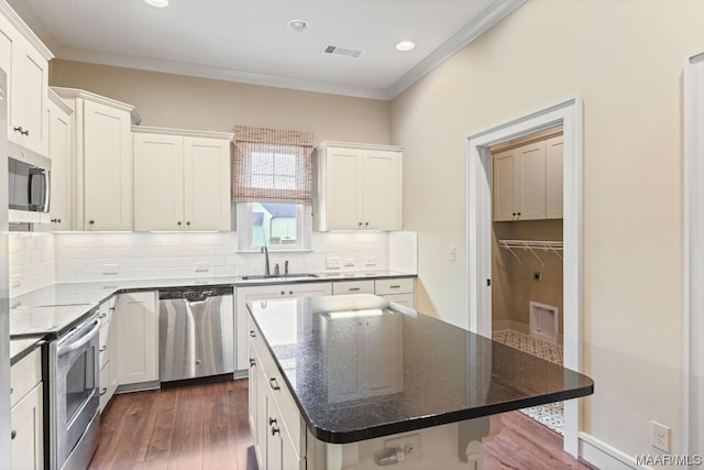 kitchen featuring dark stone counters, dark wood-type flooring, appliances with stainless steel finishes, a kitchen island, and backsplash