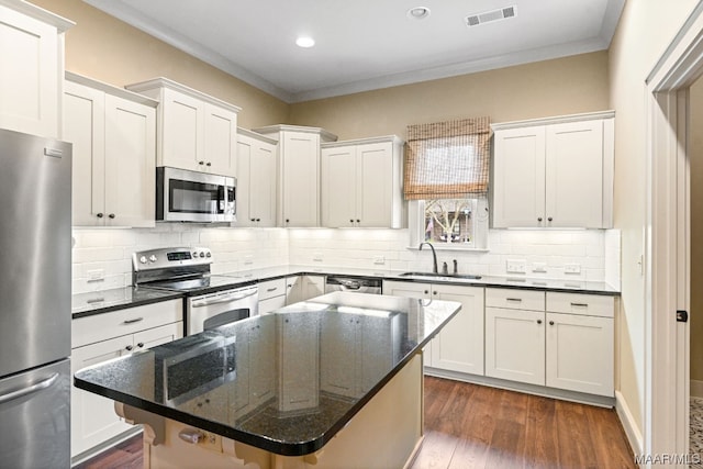 kitchen featuring appliances with stainless steel finishes, white cabinets, a center island, backsplash, and sink