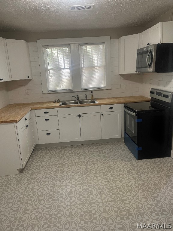 kitchen featuring appliances with stainless steel finishes, sink, light tile floors, and white cabinets