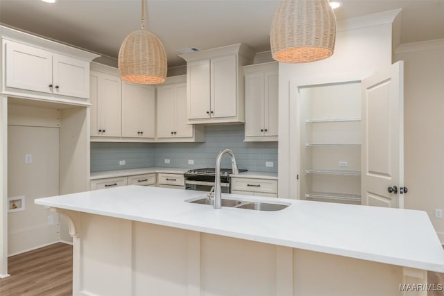 kitchen with decorative light fixtures, tasteful backsplash, white cabinetry, sink, and a center island with sink