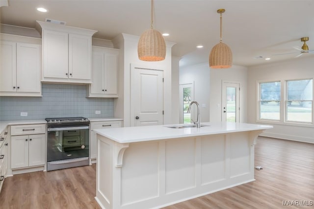 kitchen featuring sink, stainless steel stove, decorative light fixtures, and a center island with sink