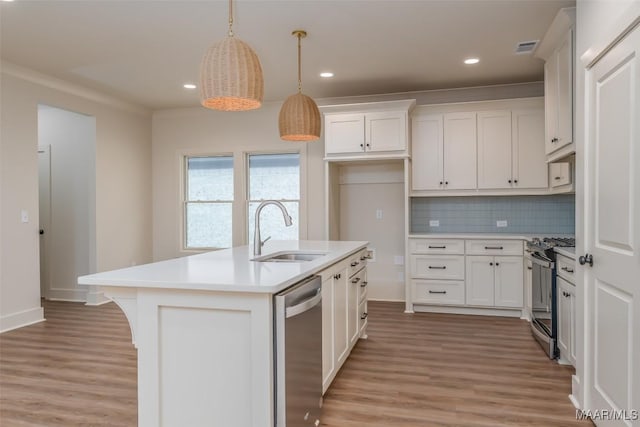 kitchen with appliances with stainless steel finishes, decorative light fixtures, an island with sink, sink, and white cabinets