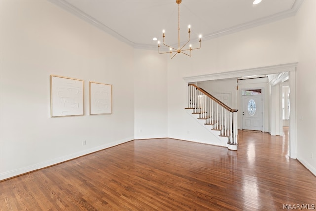 spare room featuring a notable chandelier, hardwood / wood-style flooring, ornamental molding, and a high ceiling