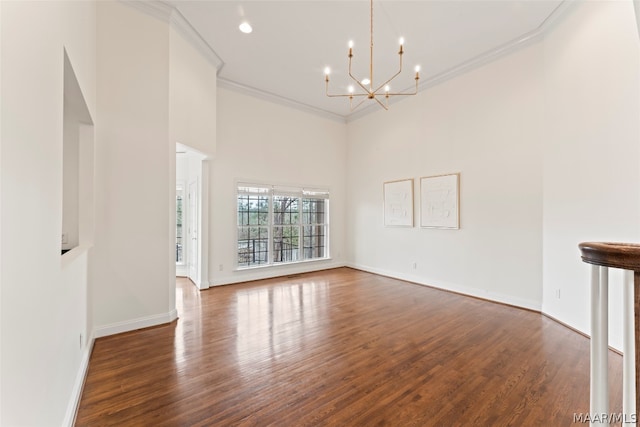 unfurnished living room with crown molding, a towering ceiling, an inviting chandelier, and dark hardwood / wood-style floors