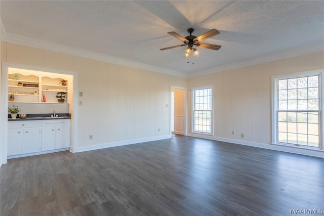 unfurnished living room with built in features, crown molding, ceiling fan, and dark hardwood / wood-style flooring