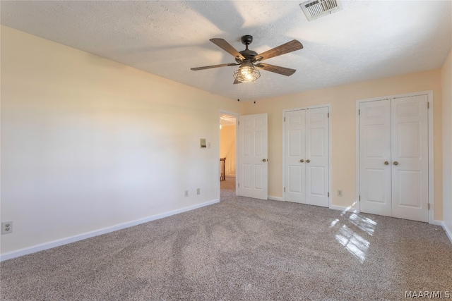 unfurnished bedroom with carpet, two closets, and ceiling fan