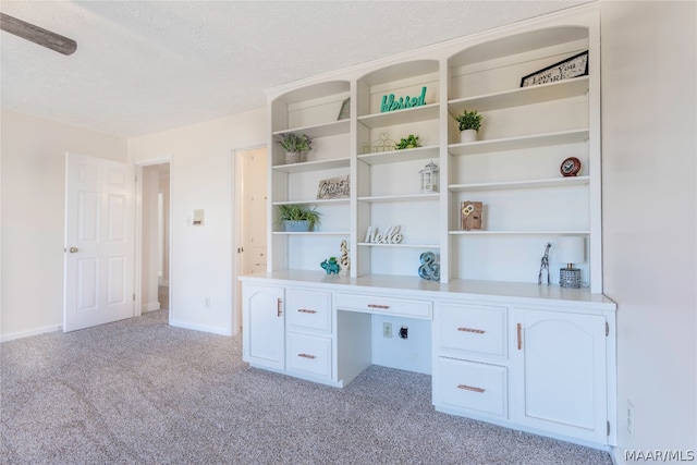 unfurnished office with a textured ceiling, light colored carpet, and built in desk