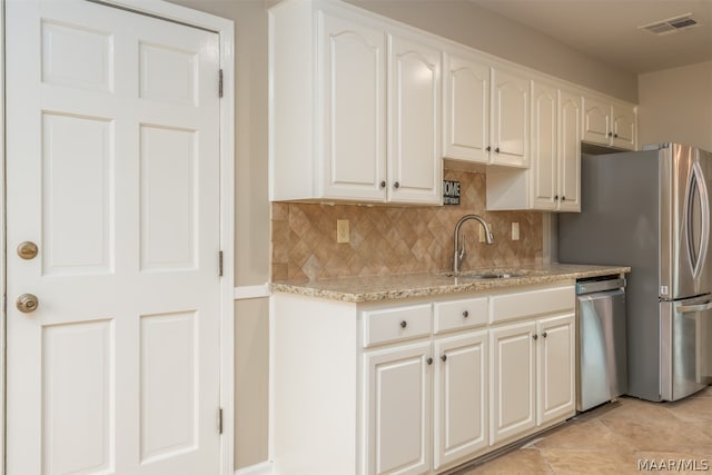 kitchen featuring white cabinets, appliances with stainless steel finishes, light stone counters, and light tile flooring