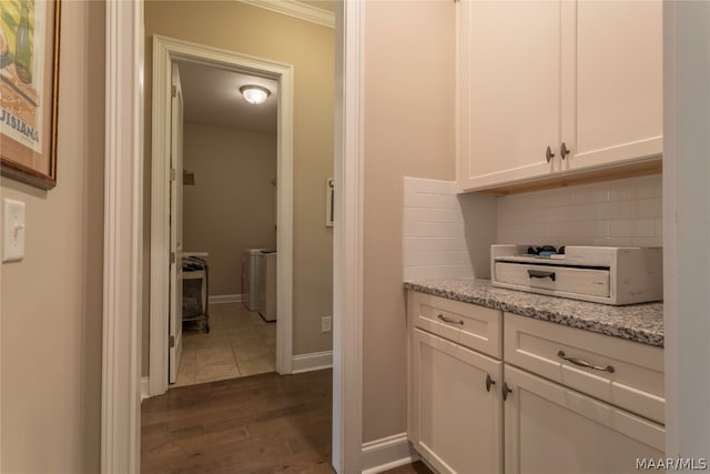 kitchen featuring ornamental molding, light stone countertops, dark wood-type flooring, tasteful backsplash, and white cabinetry