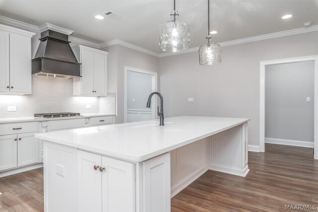 kitchen featuring premium range hood, stainless steel gas cooktop, a kitchen island with sink, white cabinets, and sink