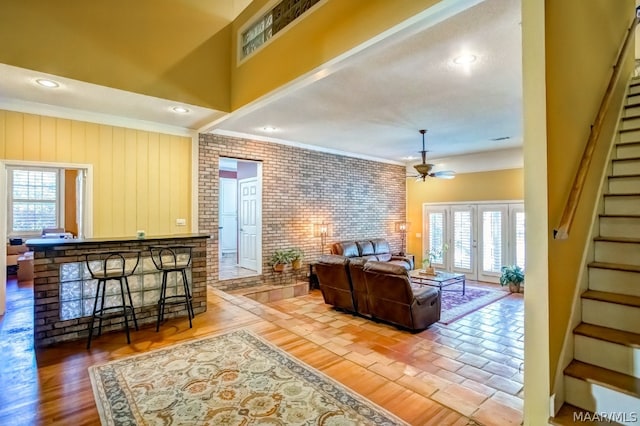 living room with ceiling fan, hardwood / wood-style floors, brick wall, ornamental molding, and french doors