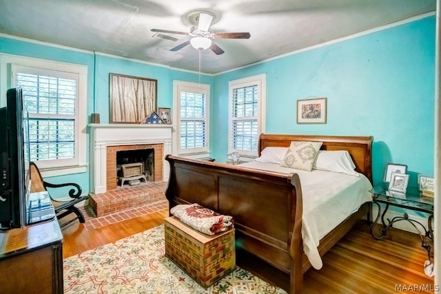 bedroom with wood-type flooring, multiple windows, a brick fireplace, and ceiling fan