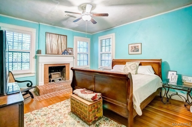 bedroom featuring ceiling fan, multiple windows, a brick fireplace, and hardwood / wood-style floors