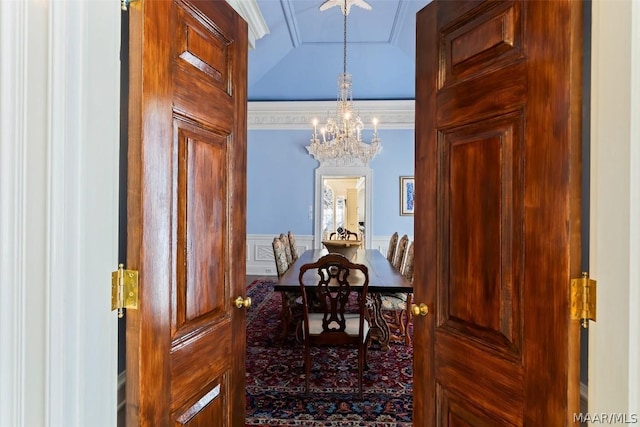 dining space featuring a wainscoted wall, lofted ceiling, a decorative wall, an inviting chandelier, and ornamental molding