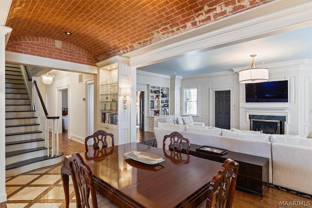 dining area featuring baseboards, a premium fireplace, stairway, brick ceiling, and vaulted ceiling