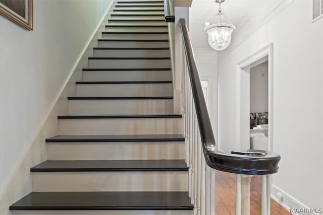 staircase with visible vents, a notable chandelier, wood finished floors, crown molding, and baseboards