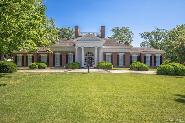 greek revival house with a front yard, brick siding, and a chimney