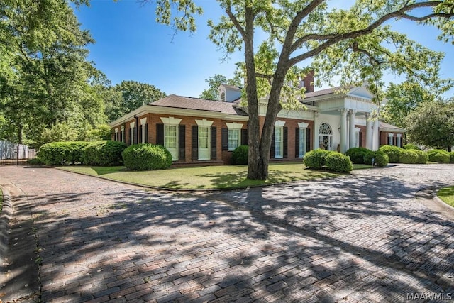 greek revival inspired property with brick siding, a front yard, and fence