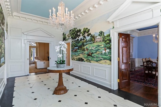 foyer entrance featuring a notable chandelier, a decorative wall, ornamental molding, wainscoting, and wood finished floors