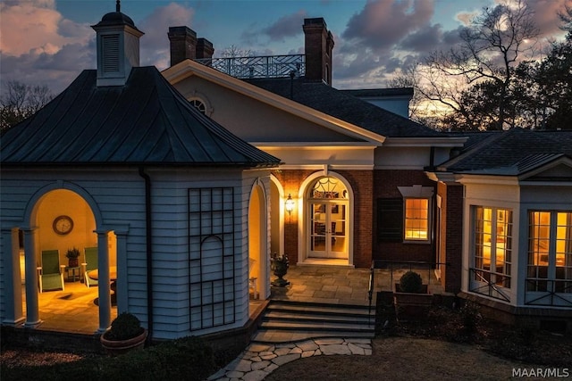 view of front of home featuring a standing seam roof, brick siding, metal roof, and french doors