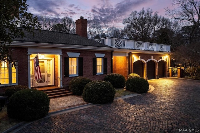 view of front of property with brick siding, decorative driveway, a chimney, and a balcony