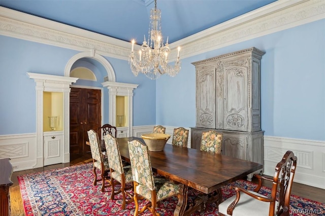 dining area featuring a wainscoted wall, decorative columns, ornamental molding, wood finished floors, and a chandelier