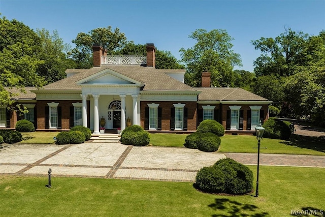 greek revival house featuring brick siding, a chimney, and a front yard