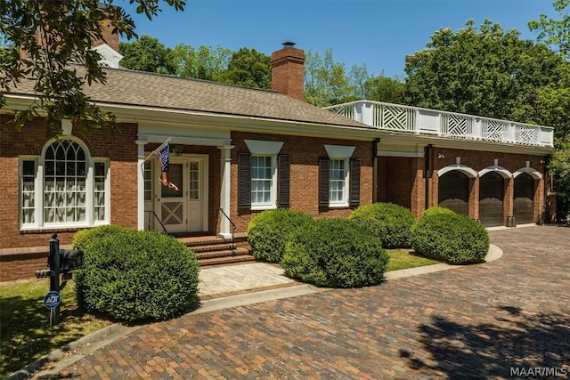 view of front of house with a chimney, roof with shingles, an attached garage, decorative driveway, and brick siding