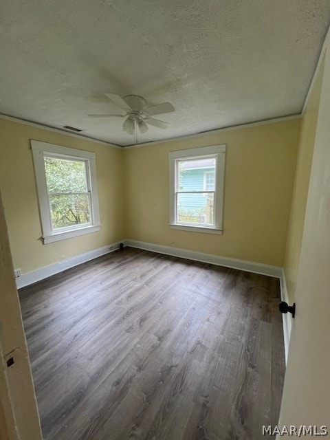 empty room featuring a wealth of natural light, dark hardwood / wood-style flooring, ceiling fan, and a textured ceiling