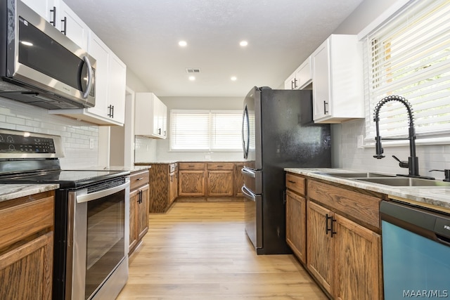 kitchen with appliances with stainless steel finishes, light wood-type flooring, a wealth of natural light, and white cabinetry