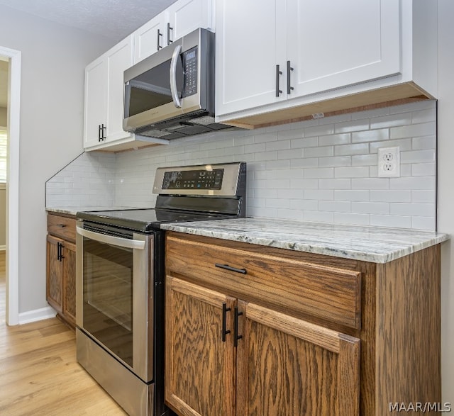 kitchen with white cabinets, stainless steel appliances, light hardwood / wood-style flooring, and tasteful backsplash