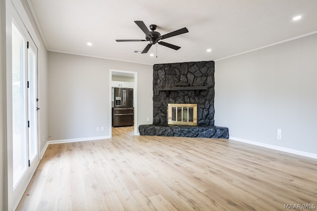 unfurnished living room with light hardwood / wood-style flooring, a stone fireplace, a wealth of natural light, crown molding, and ceiling fan