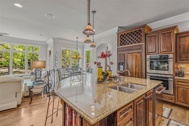 kitchen featuring decorative light fixtures, light hardwood / wood-style flooring, appliances with stainless steel finishes, sink, and an island with sink