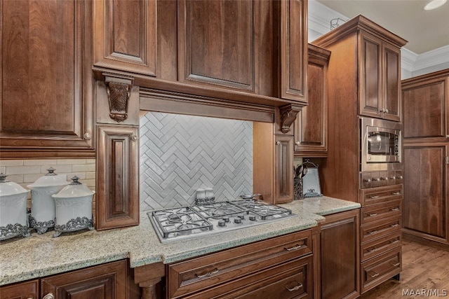 kitchen with light stone counters, backsplash, light wood-type flooring, crown molding, and stainless steel appliances