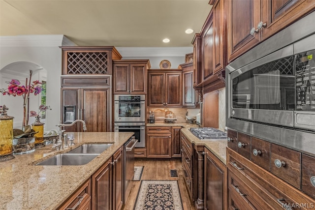 kitchen with sink, light hardwood / wood-style floors, tasteful backsplash, built in appliances, and light stone countertops