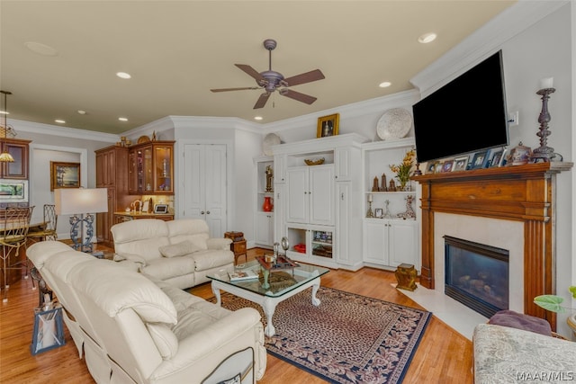 living room with crown molding, light hardwood / wood-style flooring, a tiled fireplace, and ceiling fan