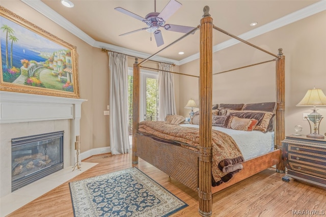 bedroom featuring a fireplace, ceiling fan, crown molding, and light wood-type flooring