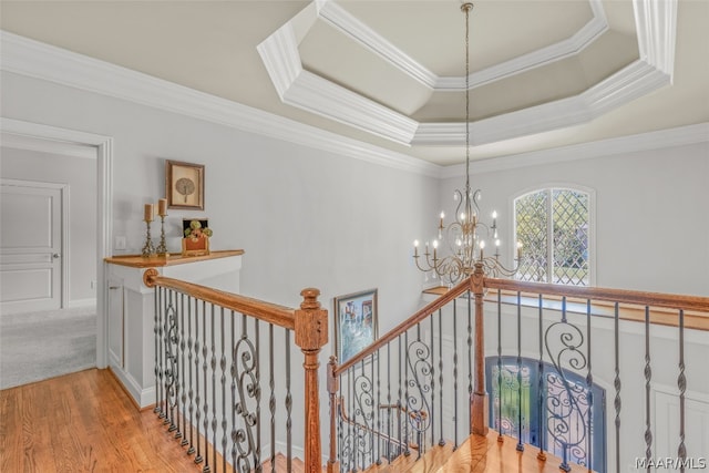 hall with light hardwood / wood-style floors, a chandelier, a raised ceiling, and crown molding